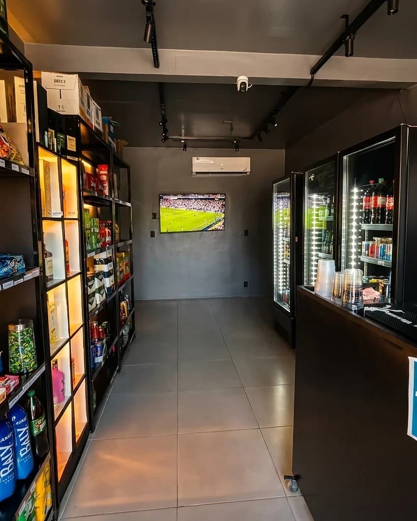 Corredor da loja com as geladeiras de cerveja acesas e a TV com o cardápio